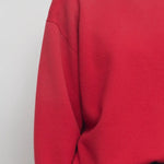 Front closeup view of red leora sweatshirt on model wearing navy pants, against a white background.