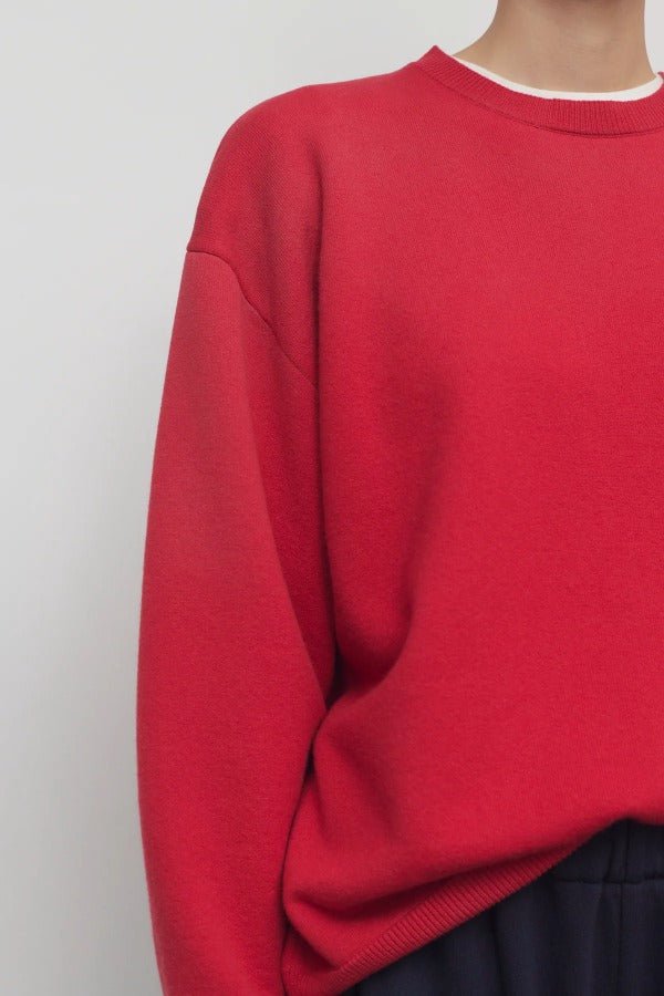 Front closeup view of red leora sweatshirt on model wearing navy pants, against a white background.