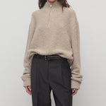 Front view of beige lethara sweater on model wearing black pants and a brown belt, against a white background.