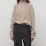 Front view of beige lethara sweater on model wearing black pants and a brown belt, against a white background.