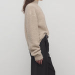Side view of beige lethara sweater on model wearing black pants, against a white background.