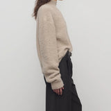 Side view of beige lethara sweater on model wearing black pants, against a white background.