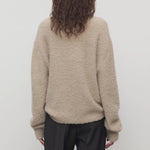 Back view of beige lethara sweater on model wearing black pants, against a white background.
