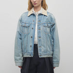 Front view of light denim collared jacket on model wearing black trousers and a white collared shirt, against a white background.