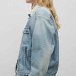 Side view of light denim collared jacket on model wearing black trousers and a white collared shirt, against a white background.