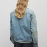 Back view of light denim collared jacket on model wearing black trousers and white collared shirt, against a white background.