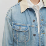 Front closeup view of light denim jacket on model wearing white collared shirt, against a white background.