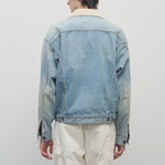 Back view of light indigo collared joret jacket on model wearing white trousers, against a white background.