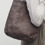 Front view of brown lilou woven tote on model wearing light stripe shirt and khaki pants against a white background.
