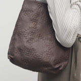 Front view of brown lilou woven tote on model wearing light stripe shirt and khaki pants against a white background.