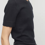 Side view of black linnea sweater on model wearing black pants and belt, against a white background.