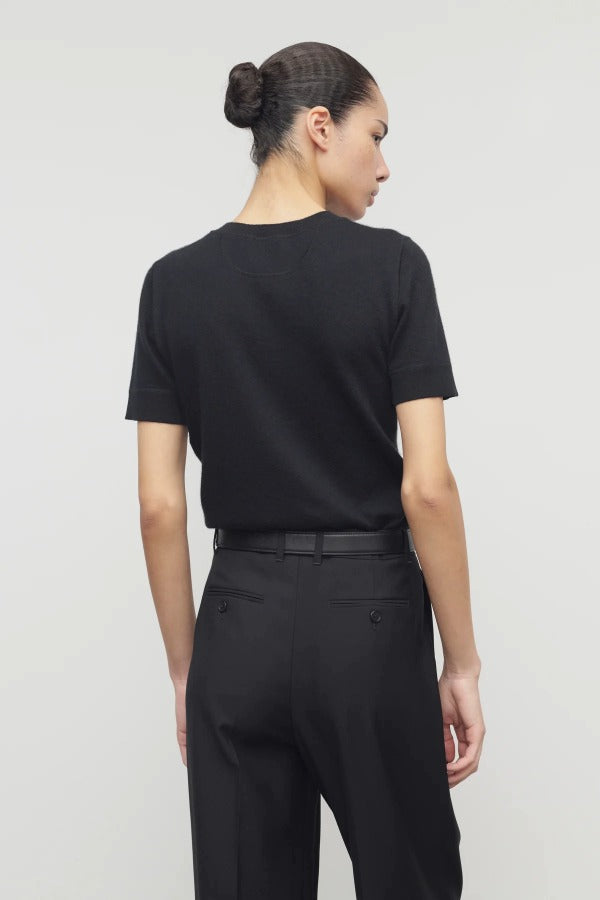 Back view of black linnea sweater on model wearing black pants and belt, against a white background.