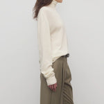 Side view of ivory lizzy top on model wearing khaki trousers and a brown belt, against a white background.