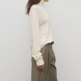 Side view of ivory lizzy top on model wearing khaki trousers and a brown belt, against a white background.