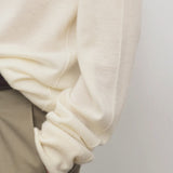 Side closeup view of ivory lizzy top on model wearing khaki trousers, against a white background.
