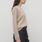 Side view of beige melange lorelei sweater on model wearing black pants and brown belt, against a white background.