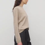 Side view of beige melange lorelei sweater on model wearing black pants and brown belt, against a white background.