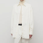 Front view of white luka shirt on model wearing white top and pants, against a white background.