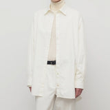 Front view of white luka shirt on model wearing white top and pants, against a white background.