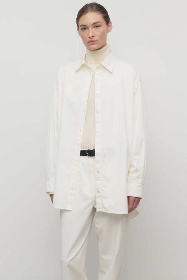 Front view of white luka shirt on model wearing white top and pants, against a white background.