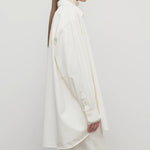 Side view of white luka shirt on model wearing white top and pants, against a white background.