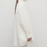 Side view of white luka shirt on model wearing white top and pants, against a white background.