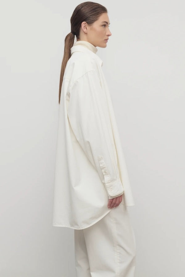 Side view of white luka shirt on model wearing white top and pants, against a white background.
