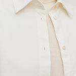 Front closeup view of white luka shirt on model wearing white top, against a white background.