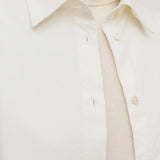Front closeup view of white luka shirt on model wearing white top, against a white background.