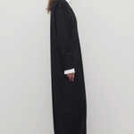 Side view of black luza dress on model wearing white collar shirt and black wedges, against a white background.