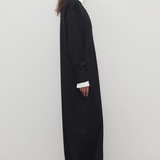 Side view of black luza dress on model wearing white collar shirt and black wedges, against a white background.