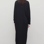 Back view of black luza dress on model wearing white collar shirt and black wedges, against a white background.
