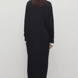 Back view of black luza dress on model wearing white collar shirt and black wedges, against a white background.
