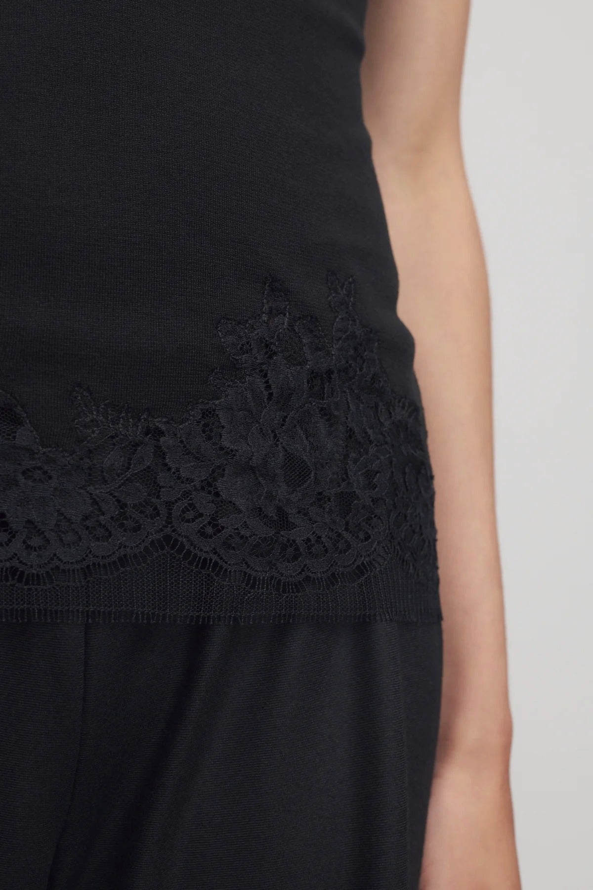 Front closeup of black makka top on model wearing black pants, against a white background.