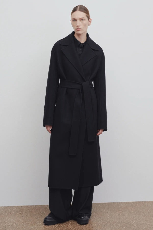 Front view of black malika coat on model wearing black pants and boots, against a white background.