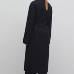 Back view of black malika coat on model wearing black pants and boots, against a white background.