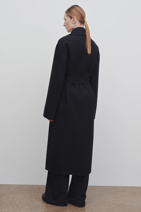 Back view of black malika coat on model wearing black pants and boots, against a white background.