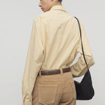 Back view of sand margan shirt on model wearing orange corduroys, brown belt and brown shoulder bag , against a white background.
