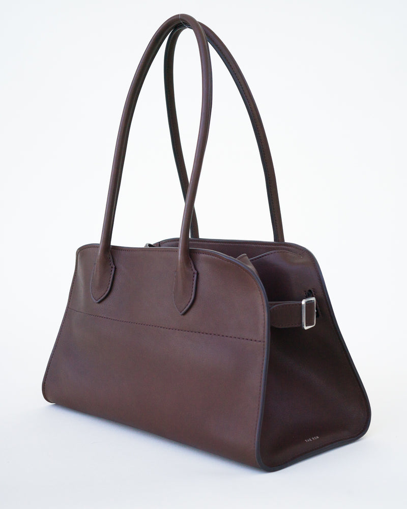 Side slanted view of brown leather bag pictured on white background, no model is shown.