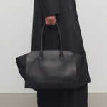 Front view of black marlo 14 bag on model wearing long black coat and boots, against a white background.