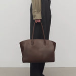 Front view of deep brown marlo 14 bag o model wearing grey pants, green shirt and mules against a white background.