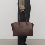 Front view of deep brown marlo 14 bag on model wearing black pants and green shirt, against a white background.