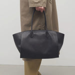 Front view of black marlo 17 bag on model wearing camel pants and khaki trench coat, against a white background.