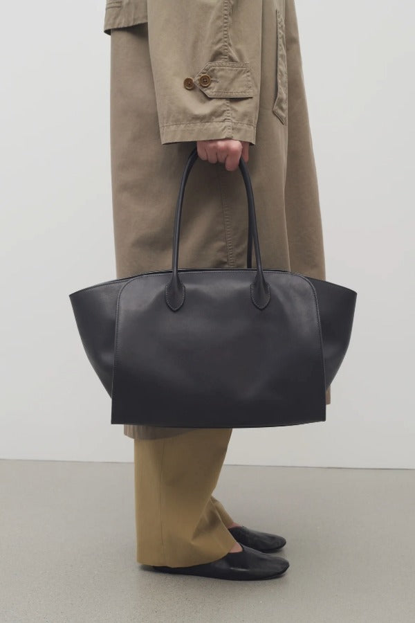 Front view of black marlo 17 bag on model wearing camel pants and khaki trench coat, against a white background.