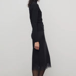 Side view of black mea skirt on model wearing black top and heels, against a white background.