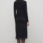 Back view of black mea skirt on model wearing black top and heels, against a white background.