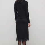 Back view of black mea skirt on model wearing black top and heels, against a white background.