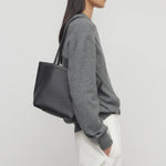Front view of black medium park tote on model wearing white pants and a grey sweater, against a white background.