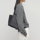 Front view of black medium park tote on model wearing white pants and a grey sweater, against a white background.