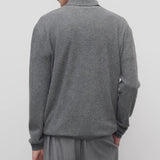 Back view of grey melange almot sweater on model wearing grey pants, against a white background.
